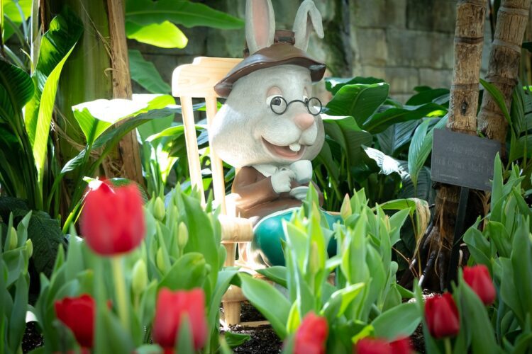 Miniature statue of a bunny in a rocking chair surrounded by flowers