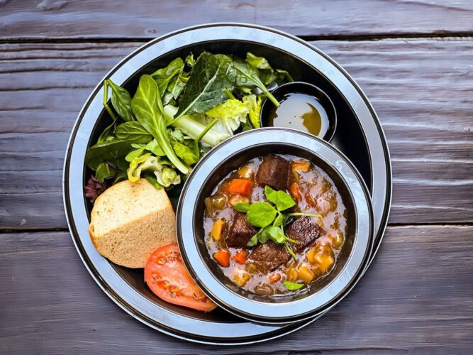 Straight-down view of plate of Irish stew with greens, tomatoes, and bread