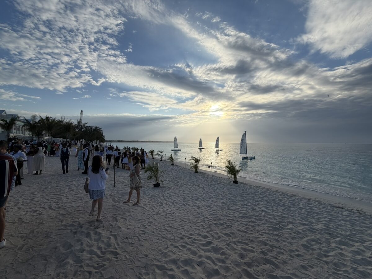 Partygoers on the beach with sailboats in the water during sunset at Beaches Turks and Caicos. 