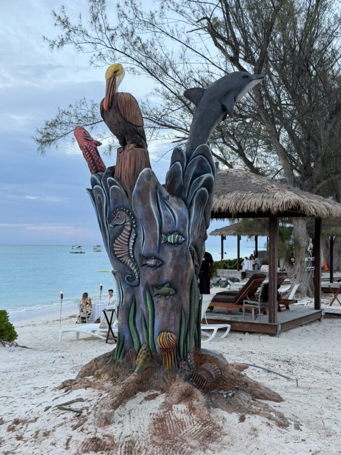 An unusual-looking tree sculpture with aquatic animals and birds on the beach.