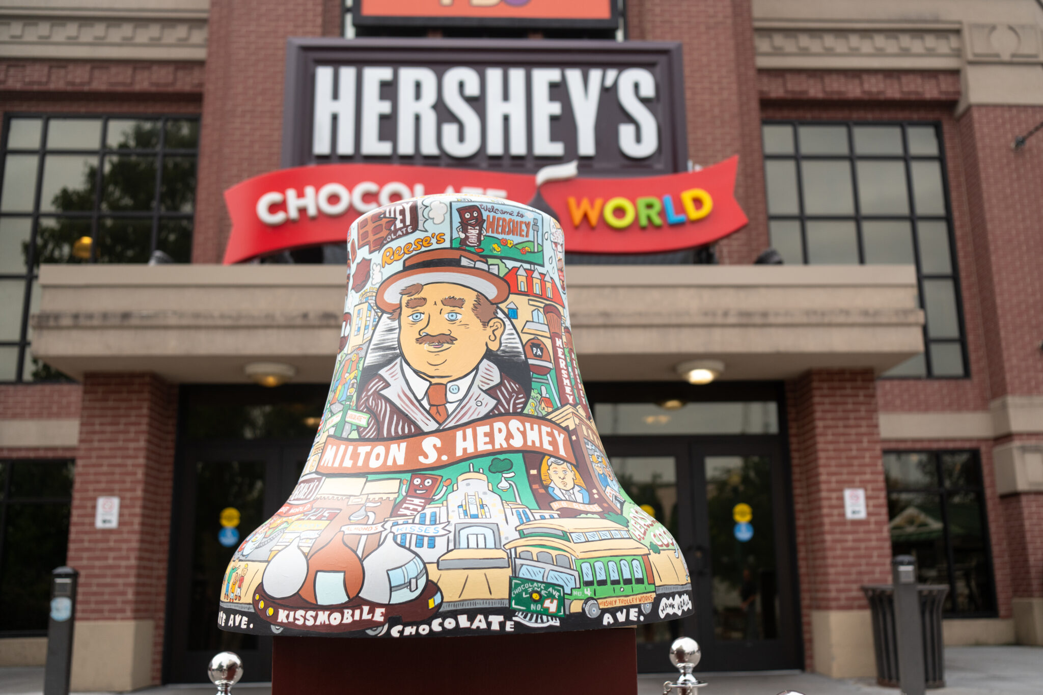 A large, illustrated Hershey’s Kiss sculpture is positioned in front of the brick entrance and main signage of Hershey's Chocolate World.