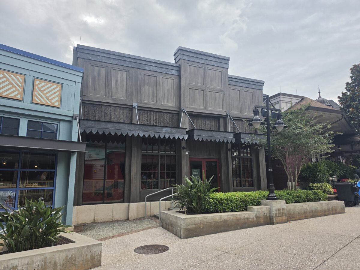 A side angle of the Six Ravens Disney Springs building windows, showing red-tinted glass reflections and a black silhouette decal of a raven wing on the window pane.