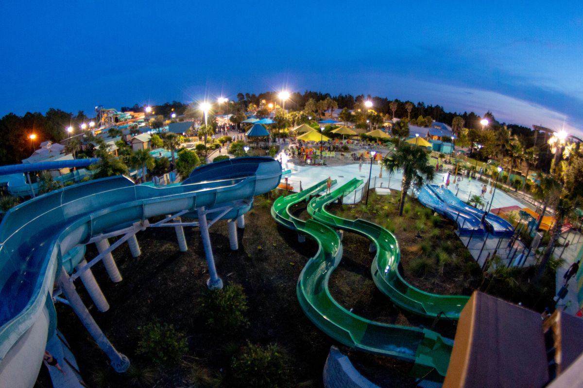Aerial view of colorful, winding waterslides illuminated under bright stadium lights during an evening waterpark event.