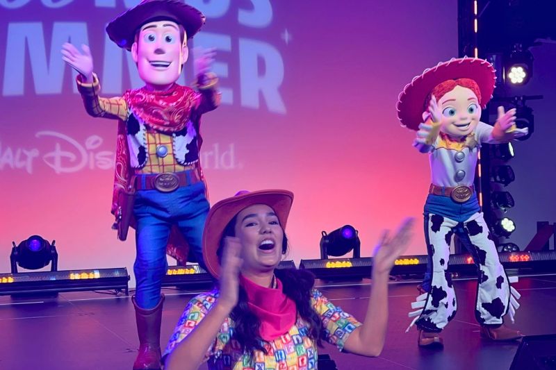 Woody and Jessie characters dancing with performer during preview of Jessie's Roundup