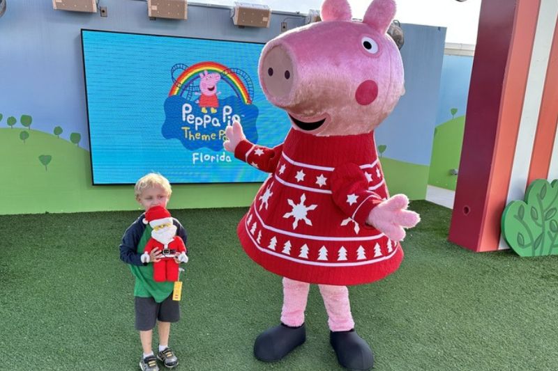 young boy with lego santa plus in hand meets Peppa Pig character during holiday event at Peppa Pig Theme Park Florida 