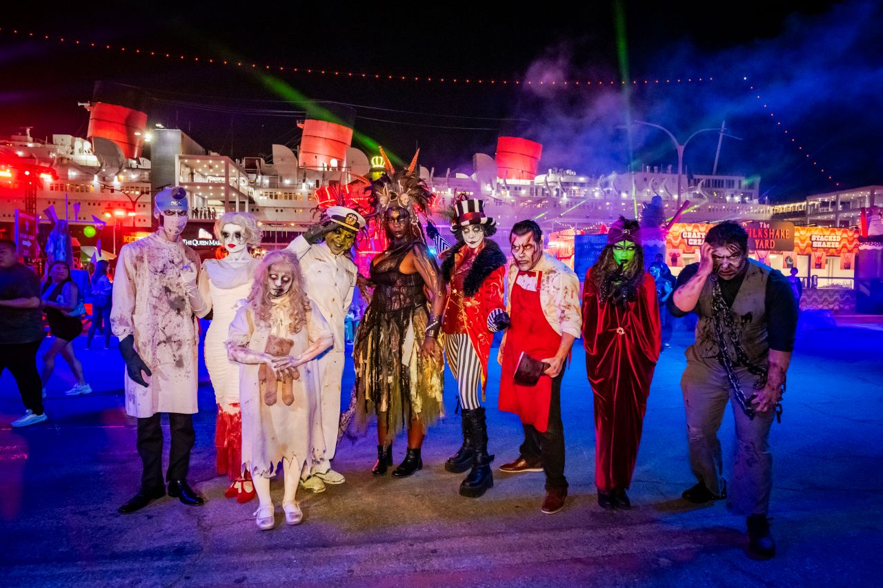 Haunted house monsters stand in front of the Queen Mary at Queen Mary's Dark Harbor Halloween event.