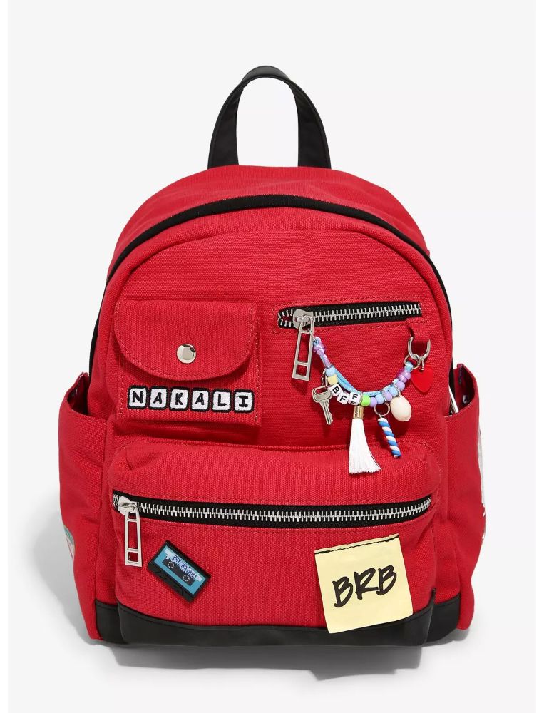 A bright red canvas backpack with a top handle, featuring a front pocket, a zippered compartment, a NAKALI patch, a BRB sticky note, and charms.