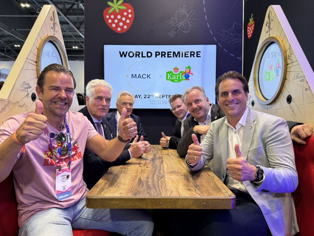 Executives posing with thumbs up, sitting at the MACK Rides FlowDiner booth vehicle display during IAAPA Europe