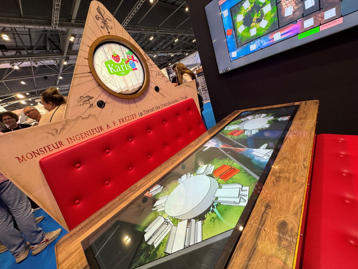 Interactive table top displaying layout graphics inside a red booth seating concept, promoting that the MACK FlowDiner opens in 2027