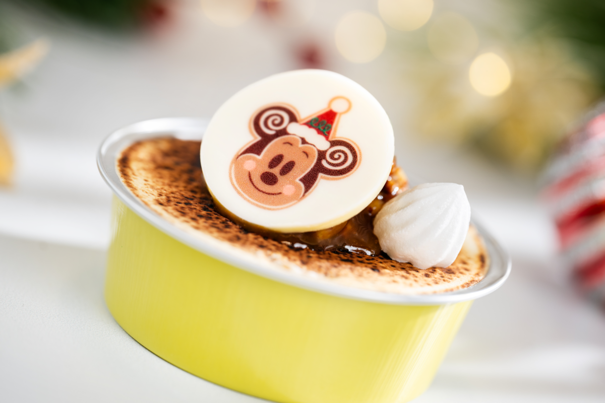 Crème brûlée dessert in a yellow ramekin topped with whipped cream and a white chocolate medallion featuring Mickey Mouse wearing a Santa hat